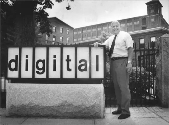Gerente posa ao lado da placa da empresa de equipamentos de computação Digital Equipment Corp.
