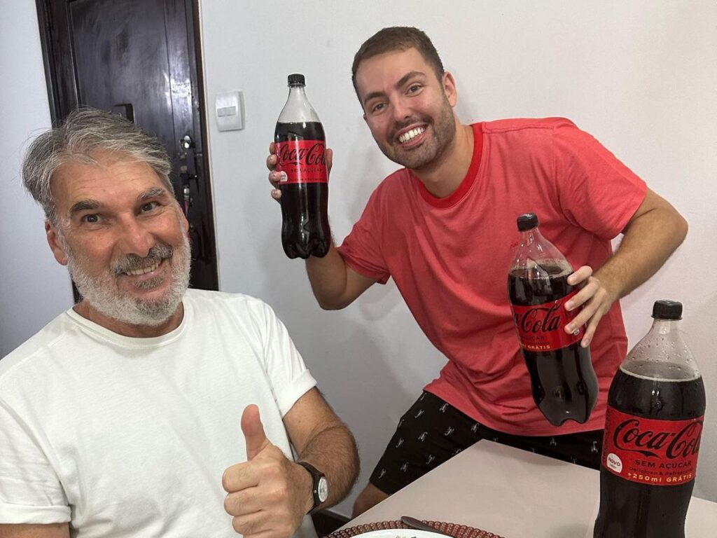 Na foto, é possível ver o influencer Matheus Costa e seu pai fazendo uma publicidade para a Coca-Cola.