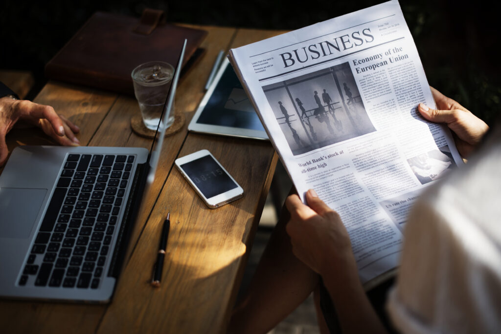 Duas pessoas em uma mesa. Uma está usando o notebook e a outra está lendo um jornal. Fonte: Freepik